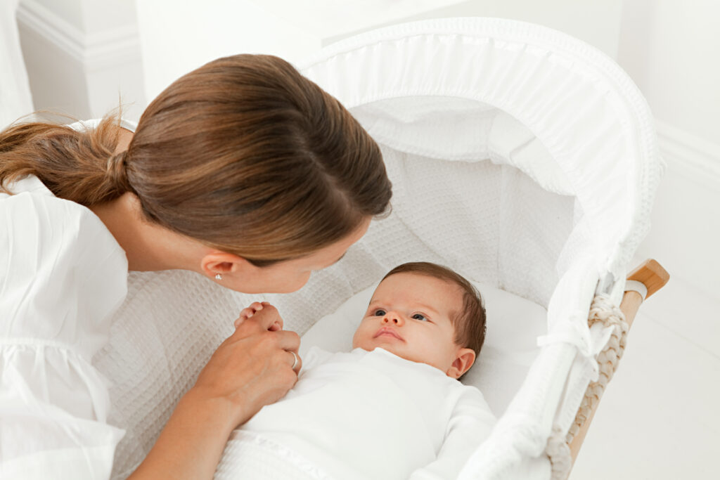 A woman is holding a baby in a white cradle.
