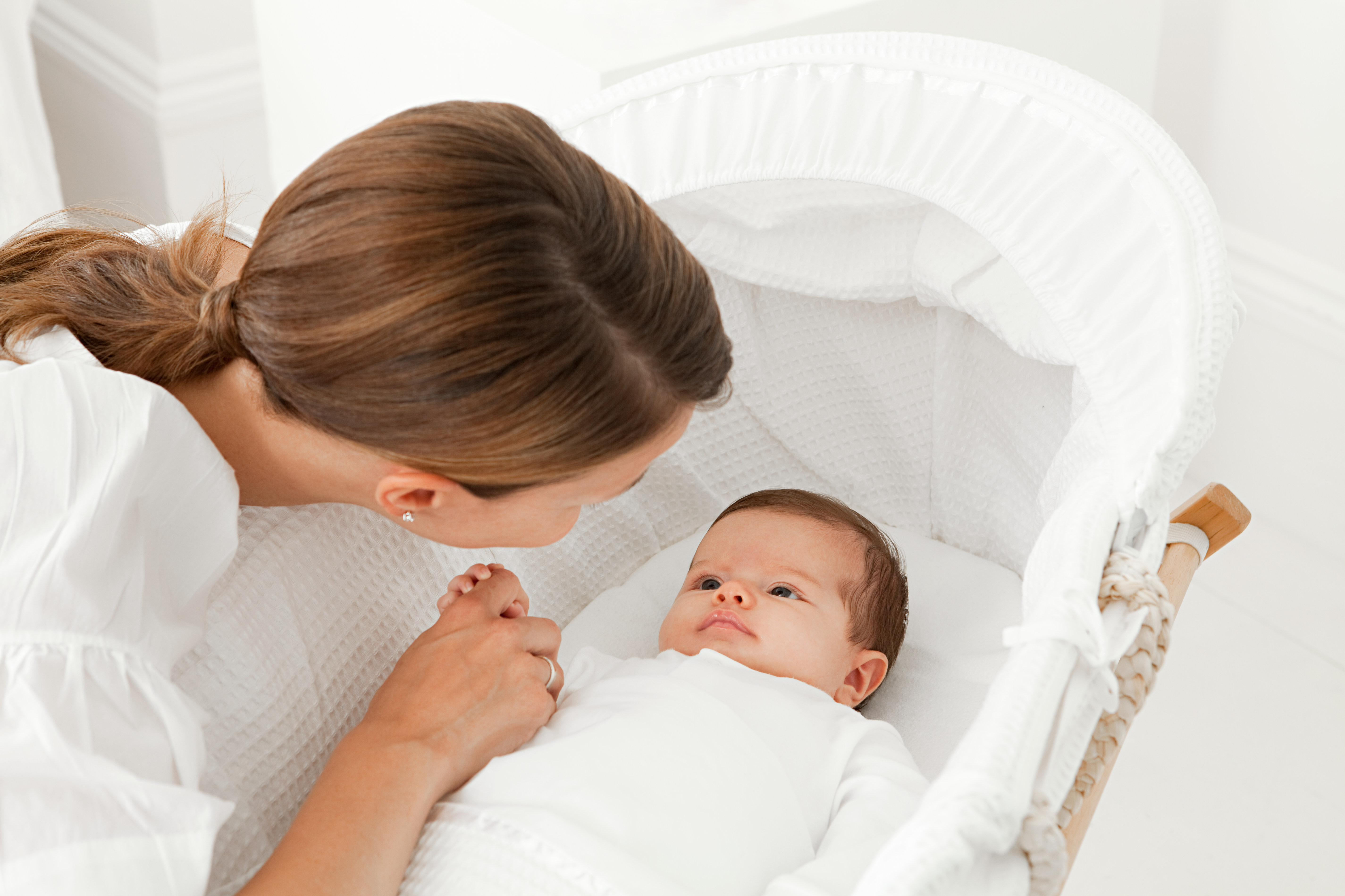 A woman is holding a baby in a white cradle.